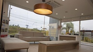 Een moderne hotellobby met een groot raam, een bank, een zitje en een receptiebalie.