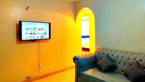 A living room with a television mounted on the wall, a sofa with patterned cushions, and a window with a decorative arch.