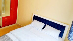 A bedroom with a bed, a red wardrobe, and a yellow wall.