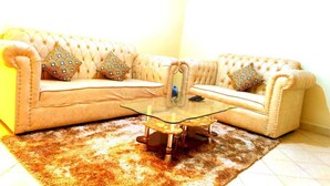 A living room with a beige sofa, patterned cushions, and a glass coffee table.