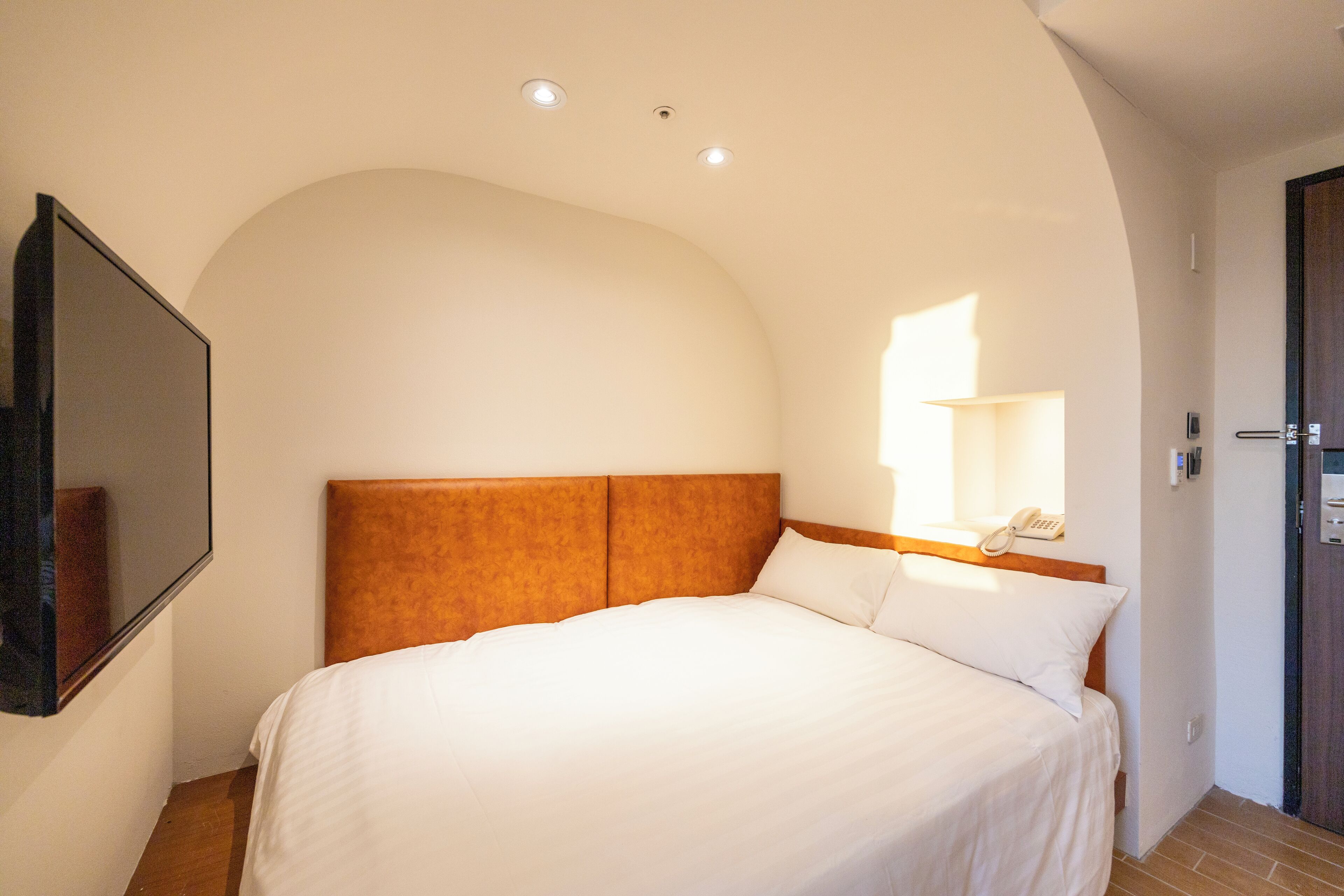 Una camera da letto con un letto grande, una testiera, un telefono sul comodino e uno specchio a parete.