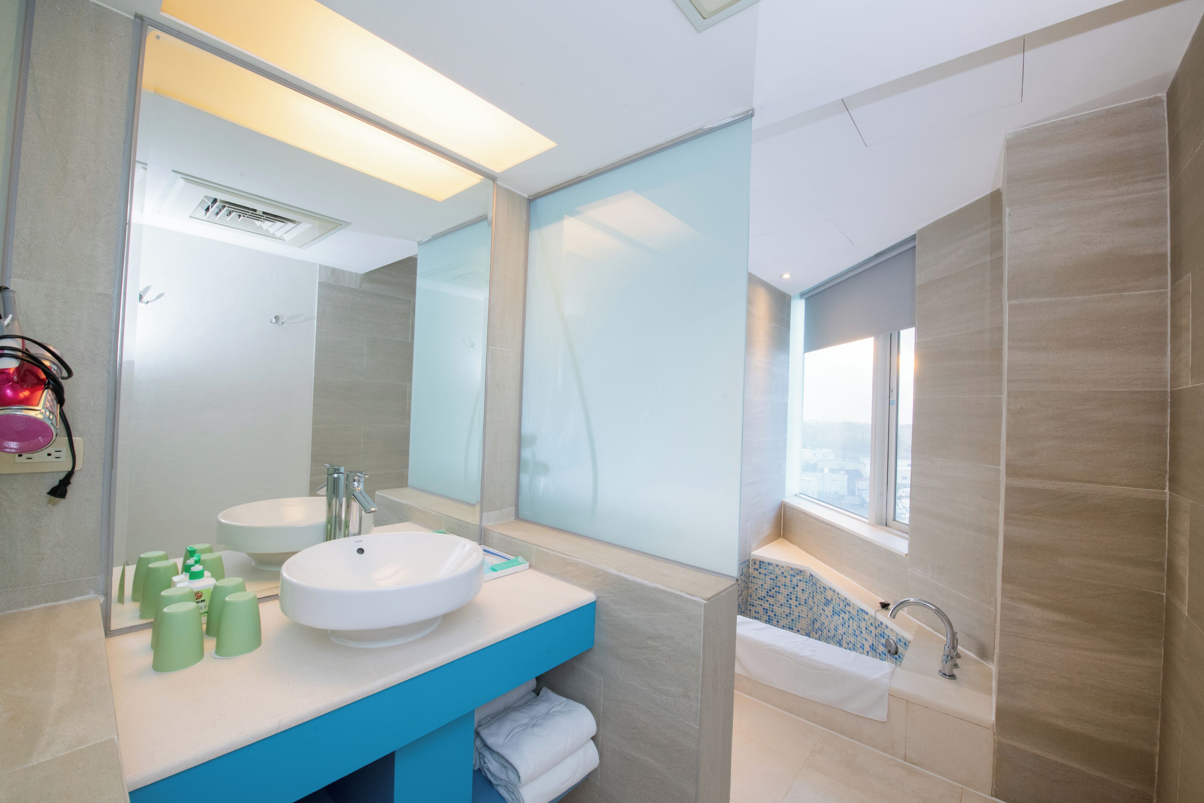 Un baño moderno con un espejo grande, un lavamanos, una bañera y una ventana con vistas.