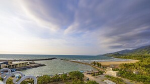A coastal view with a pier extending into the sea, a beach, and a mountainous backdrop. - Kenting Long Beach Hotel (Checheng)