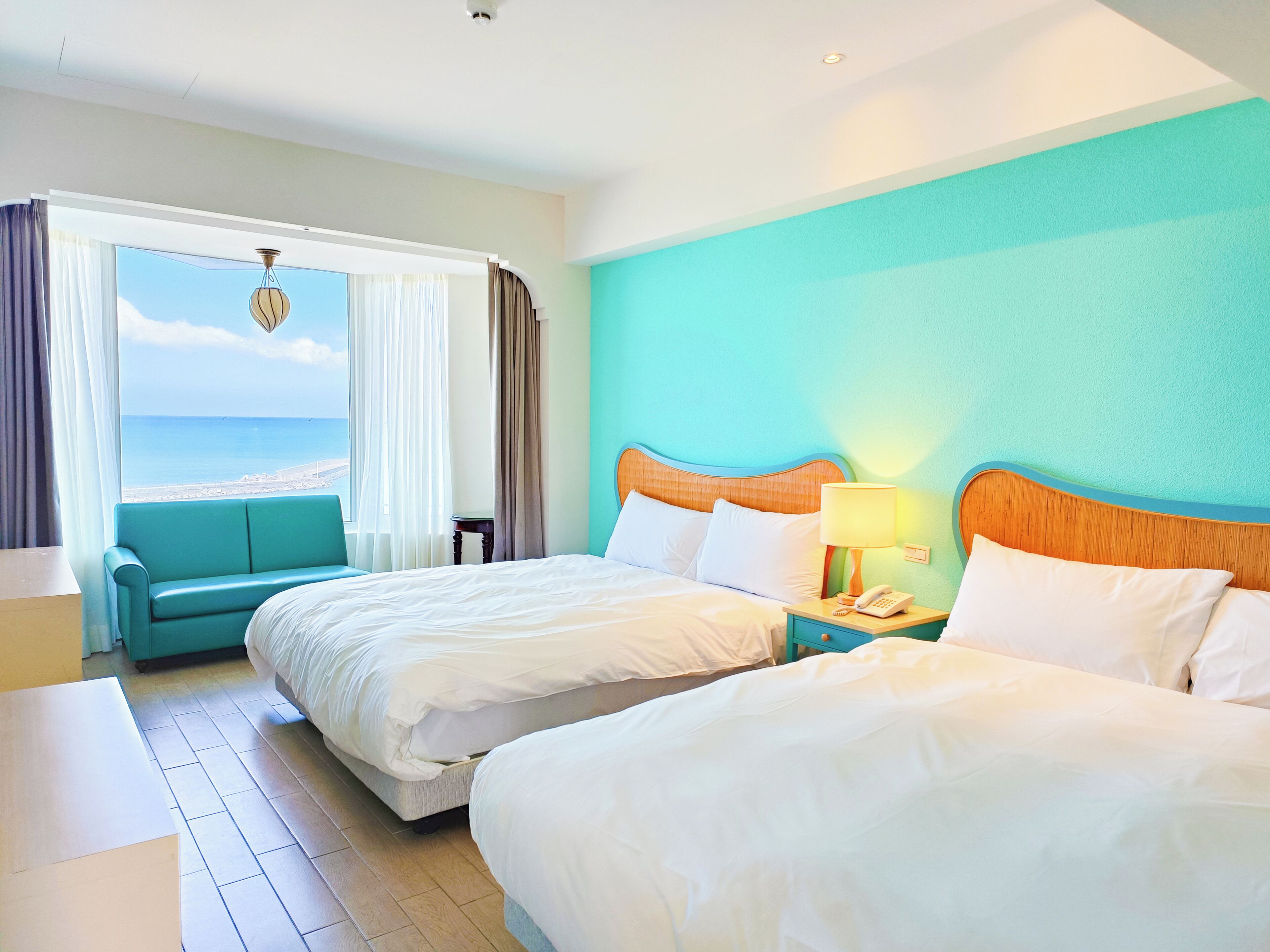 Ein Hotelzimmer mit zwei Betten und Blick auf den Strand, die Wand ist türkisblau.