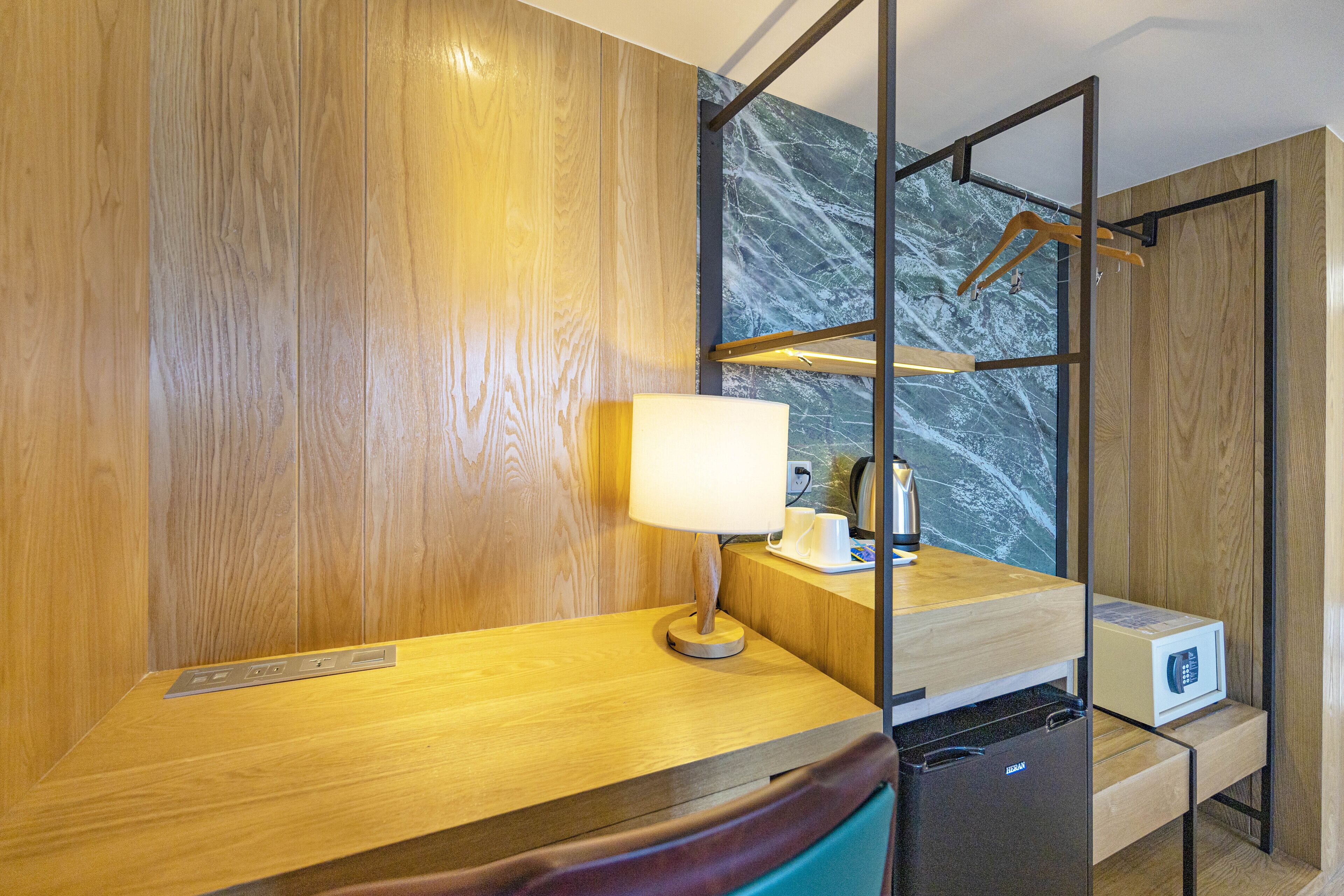 A hotel room with a wooden desk, a lamp, a microwave, and a refrigerator.