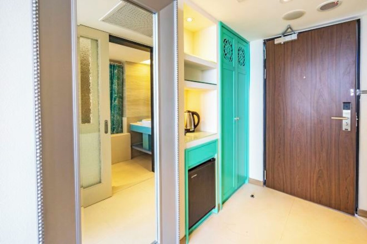 Un couloir avec un meuble de couleur turquoise, une porte en bois et un petit coin cuisine équipé d’une bouilloire.
