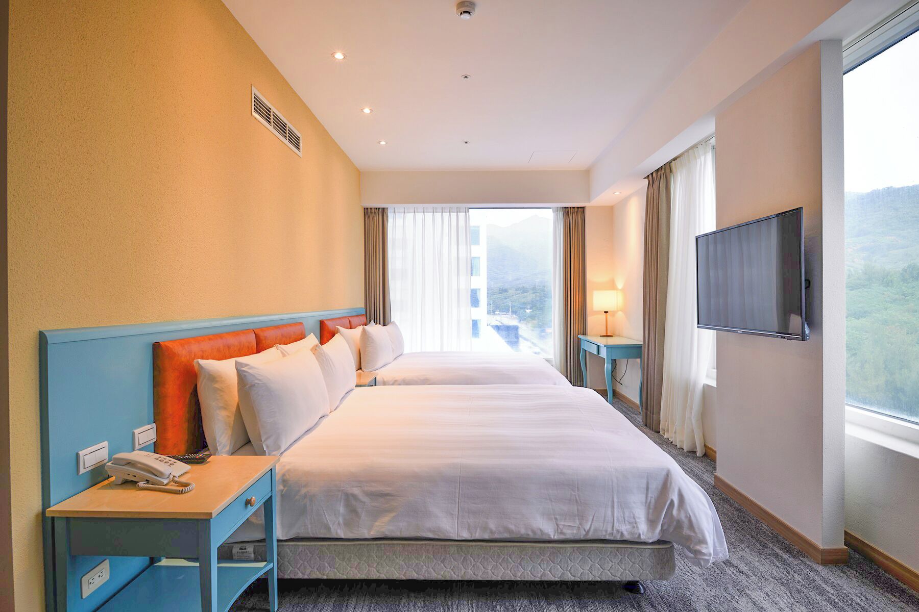 Ein Hotelzimmer mit zwei Betten, einem Fernseher, einem Telefon und Blick auf eine Berglandschaft.