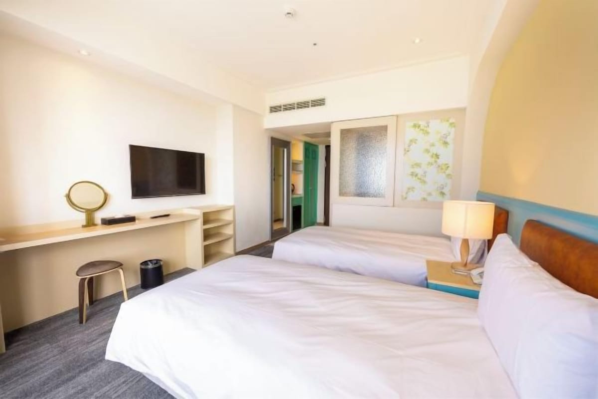 Una habitación de hotel con dos camas, un escritorio, un televisor y un espejo.