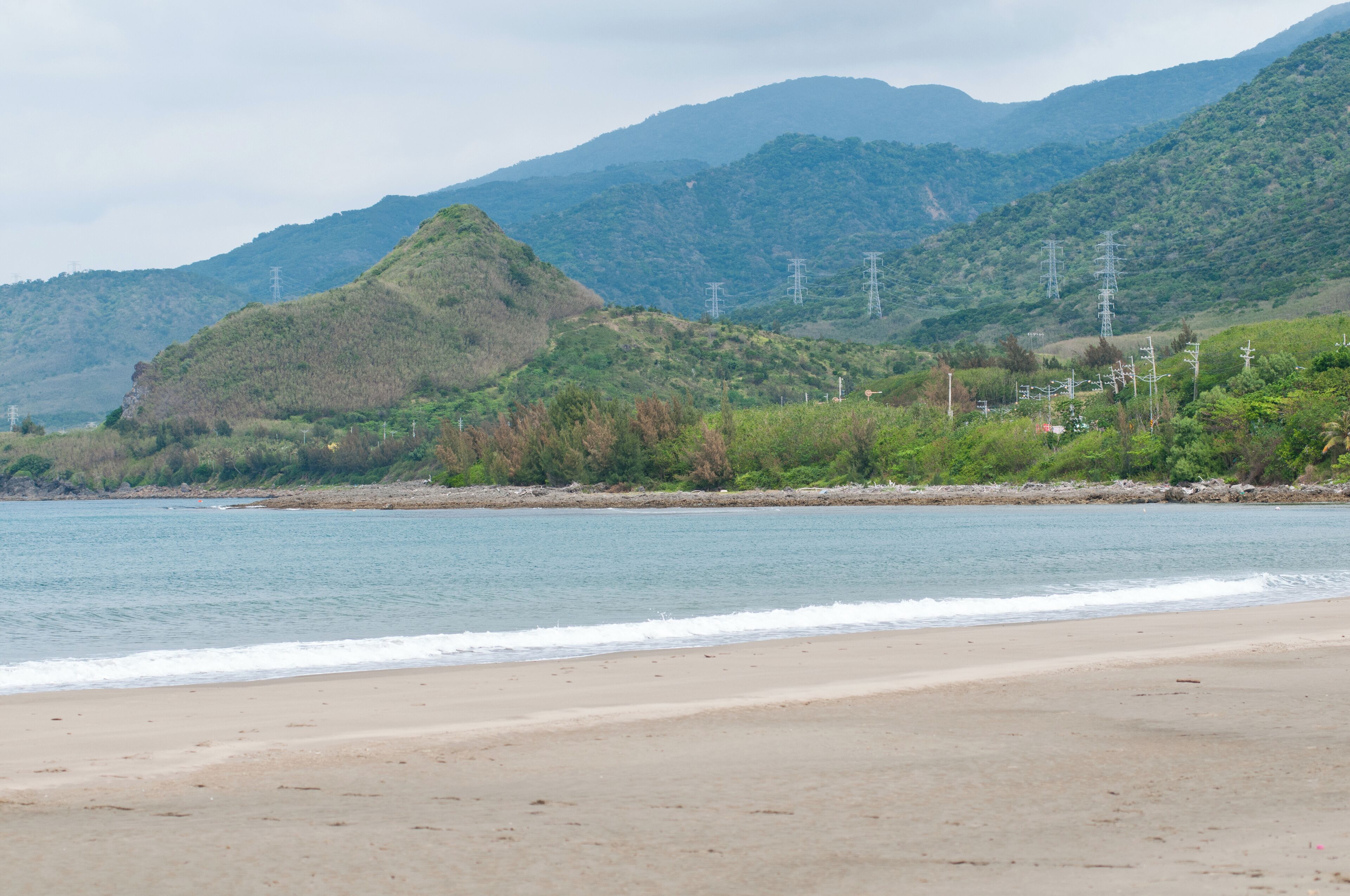 Una playa con una montaña al fondo y líneas de alta tensión.