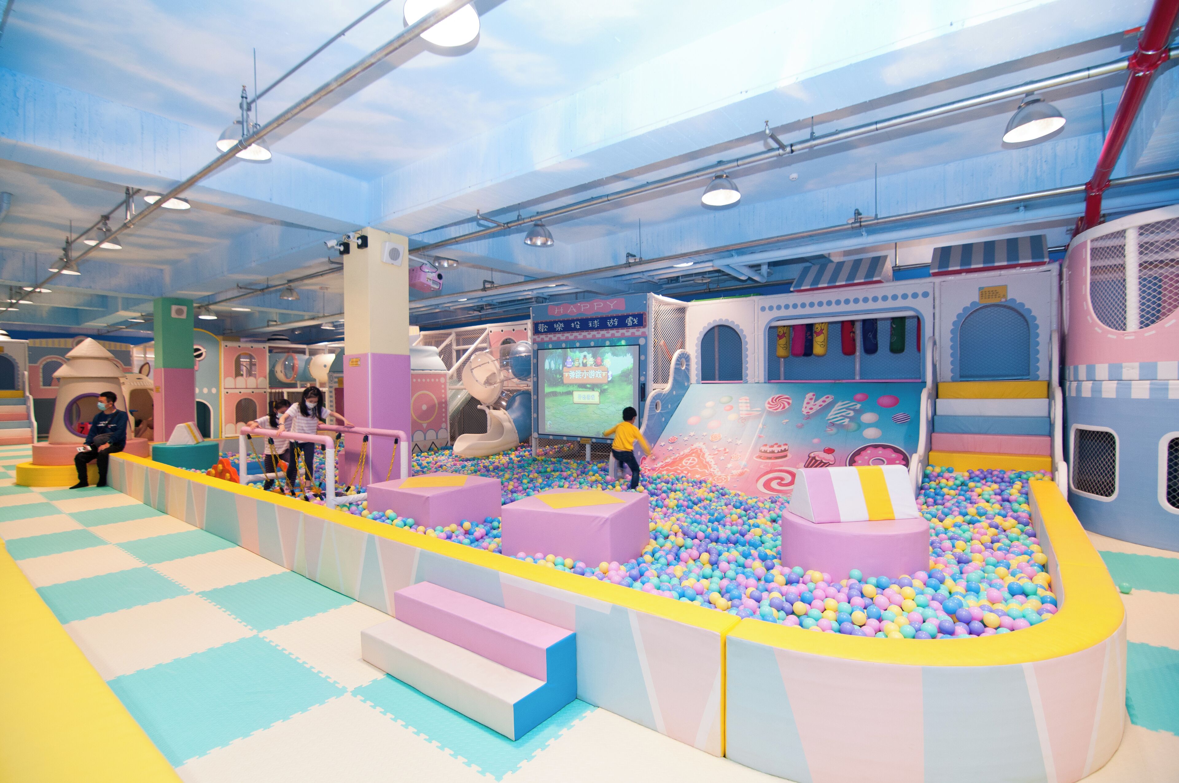 An indoor play area with colorful ball pits, play structures, and a large screen.