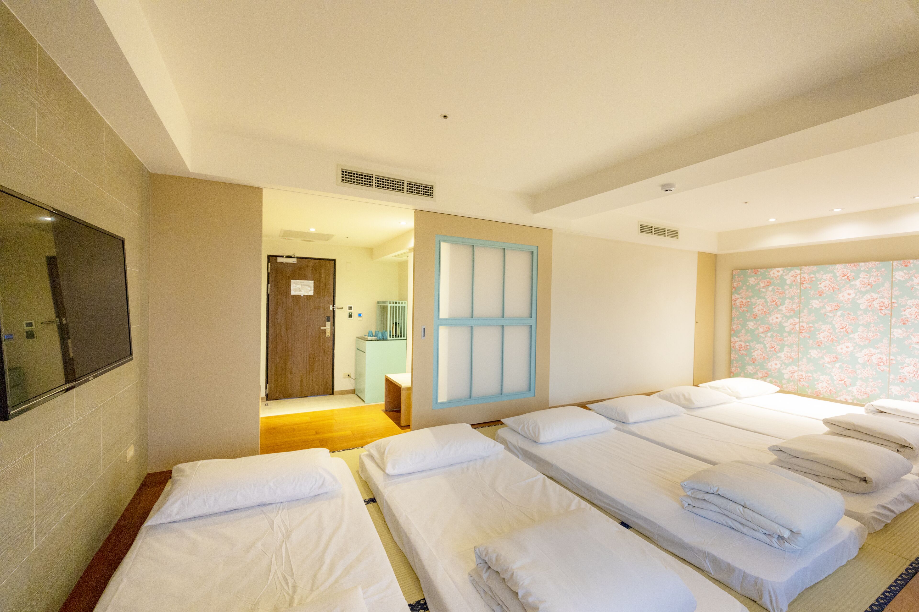 A hotel room with multiple beds, a television, and a bathroom visible through an open door.