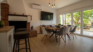 A dining area with a brick fireplace, a flat-screen TV mounted on the wall, and a large window offering a view of the outdoors. - Flora relax house (Fažana)