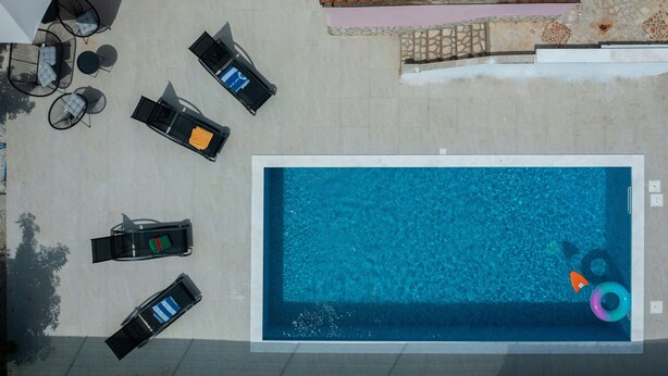 An aerial view of a swimming pool area with a rectangular pool, surrounded by black lounge chairs and a few tables. - Flora relax house (Fažana)
