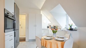 Eine moderne Küche mit weißen Schränken, einem Esstisch gedeckt mit Tellern und Gläsern sowie einem Fenster mit Blick ins Freie.