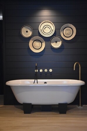 Une salle de bain moderne avec une baignoire sur pieds, un robinet doré et un lavabo noir fixé au mur.