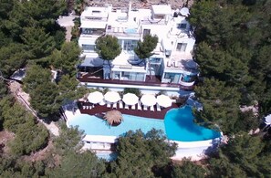 Vista aérea de un moderno complejo turístico con una piscina grande, varias tumbonas y un jardín bien cuidado.