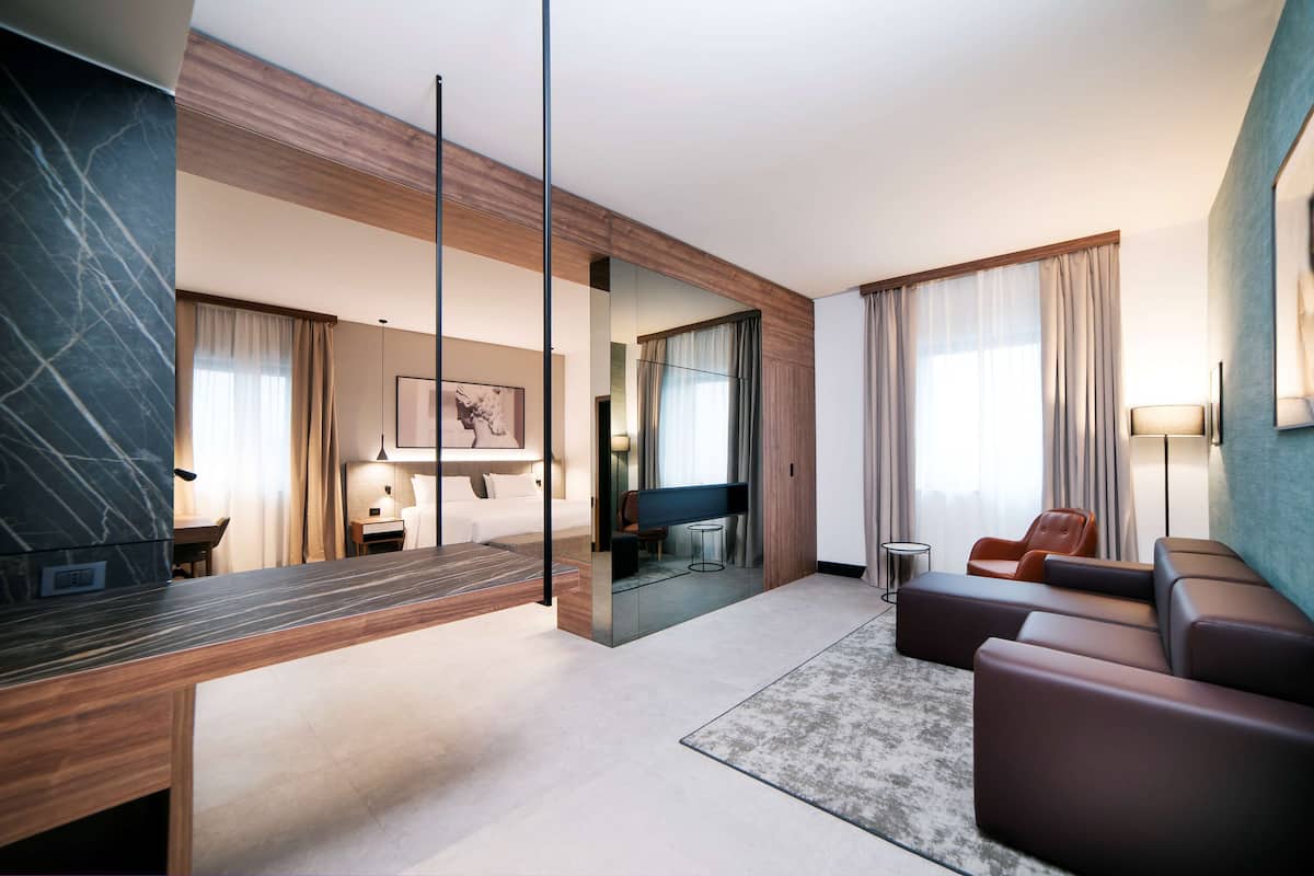 A modern hotel room with a marble accent wall, a sofa, a TV, and a large window with curtains.