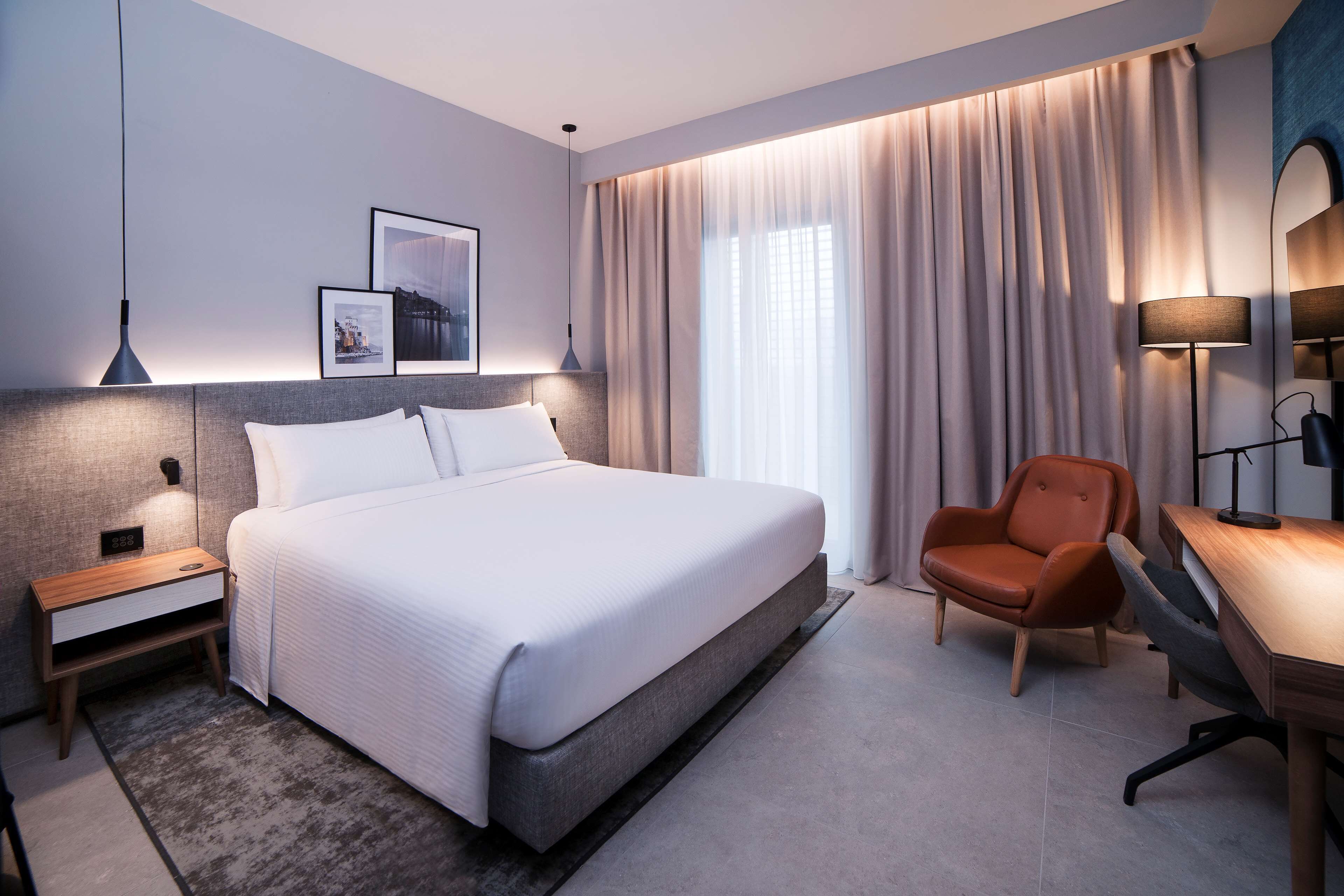 Una habitació d'hotel moderna amb un llit gran, un escriptori, una cadira i una taula de nit.