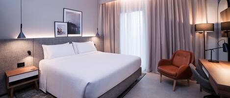 Una habitación de hotel moderna con una cama grande, un escritorio, una silla y una mesita de noche.