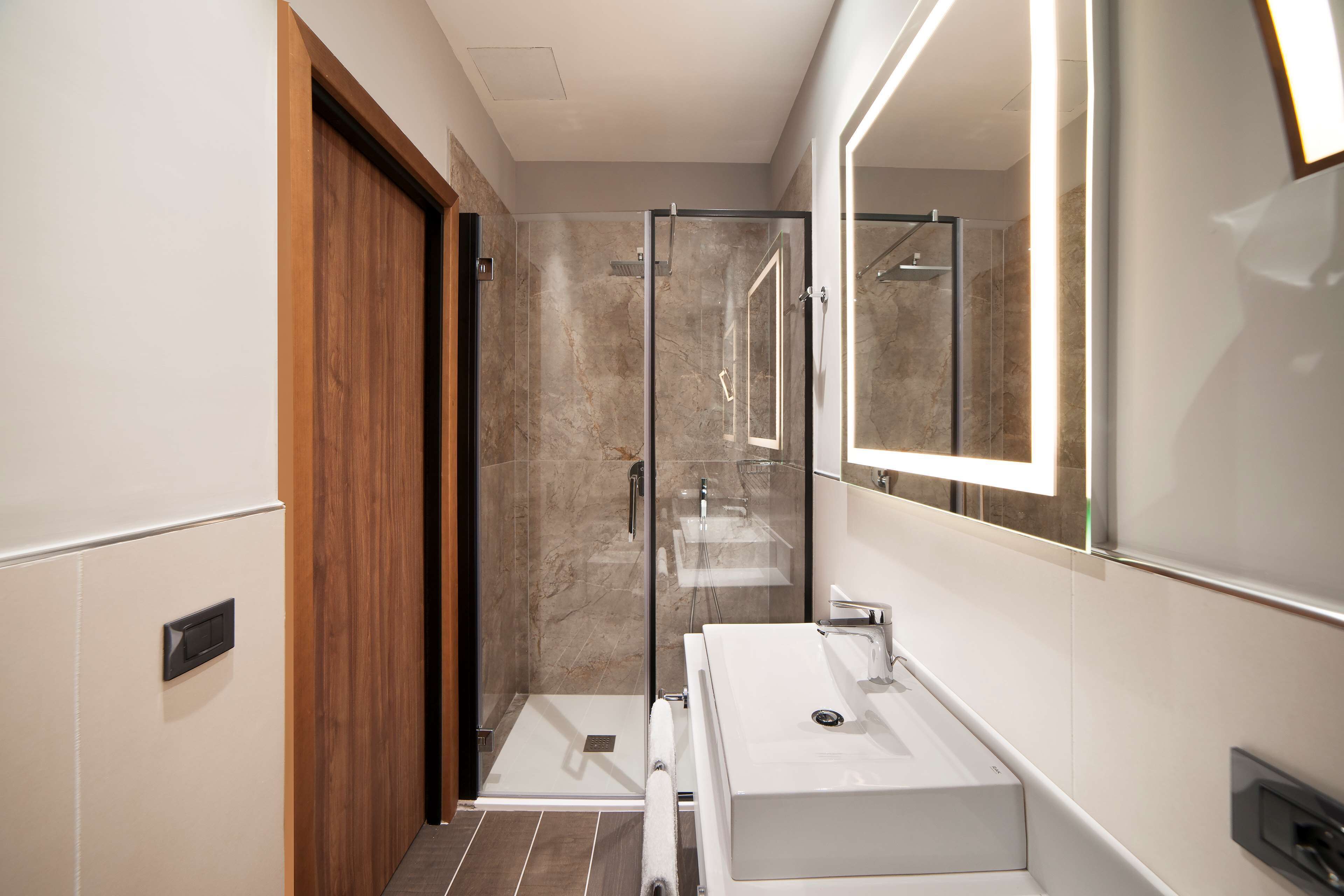 A modern bathroom with a glass-enclosed shower, a wooden door, and a large mirror.
