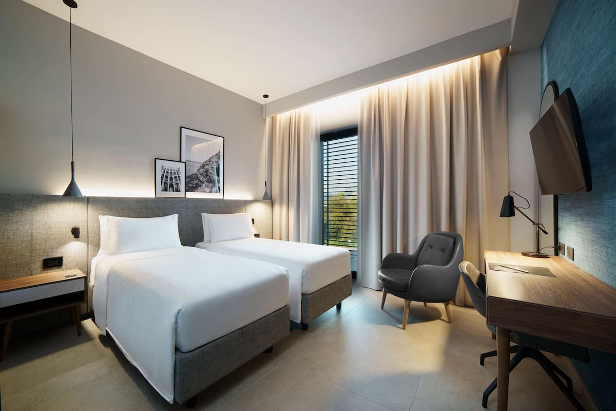 A modern hotel room with two beds, a desk, and a chair.