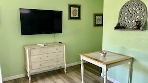 A room with a television mounted on the wall, a white dresser with drawers, and a small table with a bowl on top. - Sea Treasure - Only 2 blocks to the Beach (Cape Canaveral)