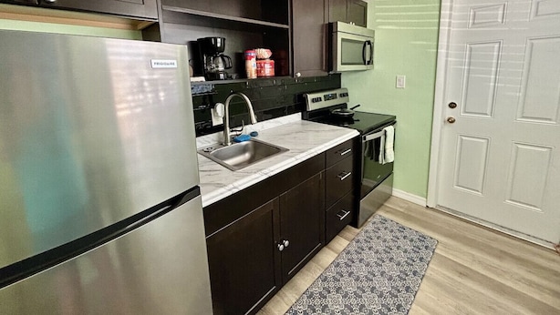A compact kitchen with dark cabinets, a stainless steel refrigerator, a microwave, and a sink. - Sea Treasure - Only 2 blocks to the Beach (Cape Canaveral)