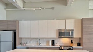 A modern kitchen with white cabinets, a stainless steel microwave, and a wooden island with two red stools.