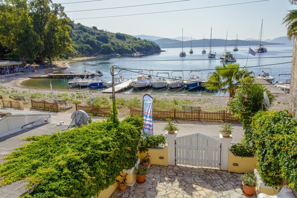 Une vue sur la côte, avec des bateaux amarrés dans une marina, le tout entouré d’une végétation luxuriante et d’un chemin de pierre menant à une entrée fermée par un portail.