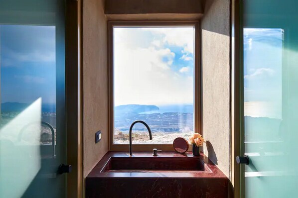 A bathroom with a sink and a window overlooking a beach. - Santorini Sky - The Lodge (Santorini)