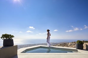 A person standing by a pool with a view of the sea and distant landscape. - Santorini Sky - The Lodge (Santorini)