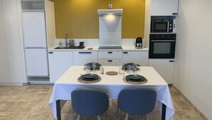 A compact kitchen with white cabinets, a microwave, an oven, and a dining table set for two with chairs.