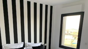 A double bed with white bedding and black pillows in a room with a striped black and white headboard.