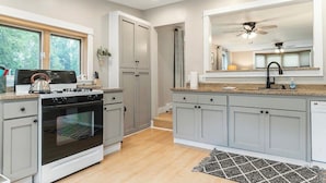 Een moderne keuken met grijze kastjes, een inbouwoven, een fornuis en een groot raam.
