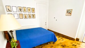 Een kamer met een bed, een lamp, een klein tafeltje met een plant en een houten vloer.