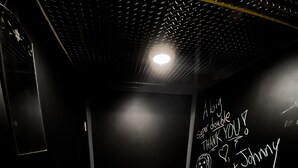 Een badkamer met een witte wasbak op een houten platform, een handzeepfles en een muur met krijt tekeningen en teksten.