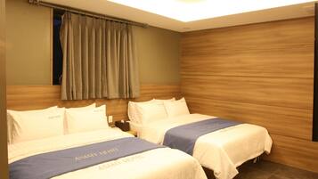 Habitación de hotel con dos camas, cada una con colcha azul y ropa de cama blanca. La habitación tiene paneles de madera en las paredes y una ventana con cortinas.