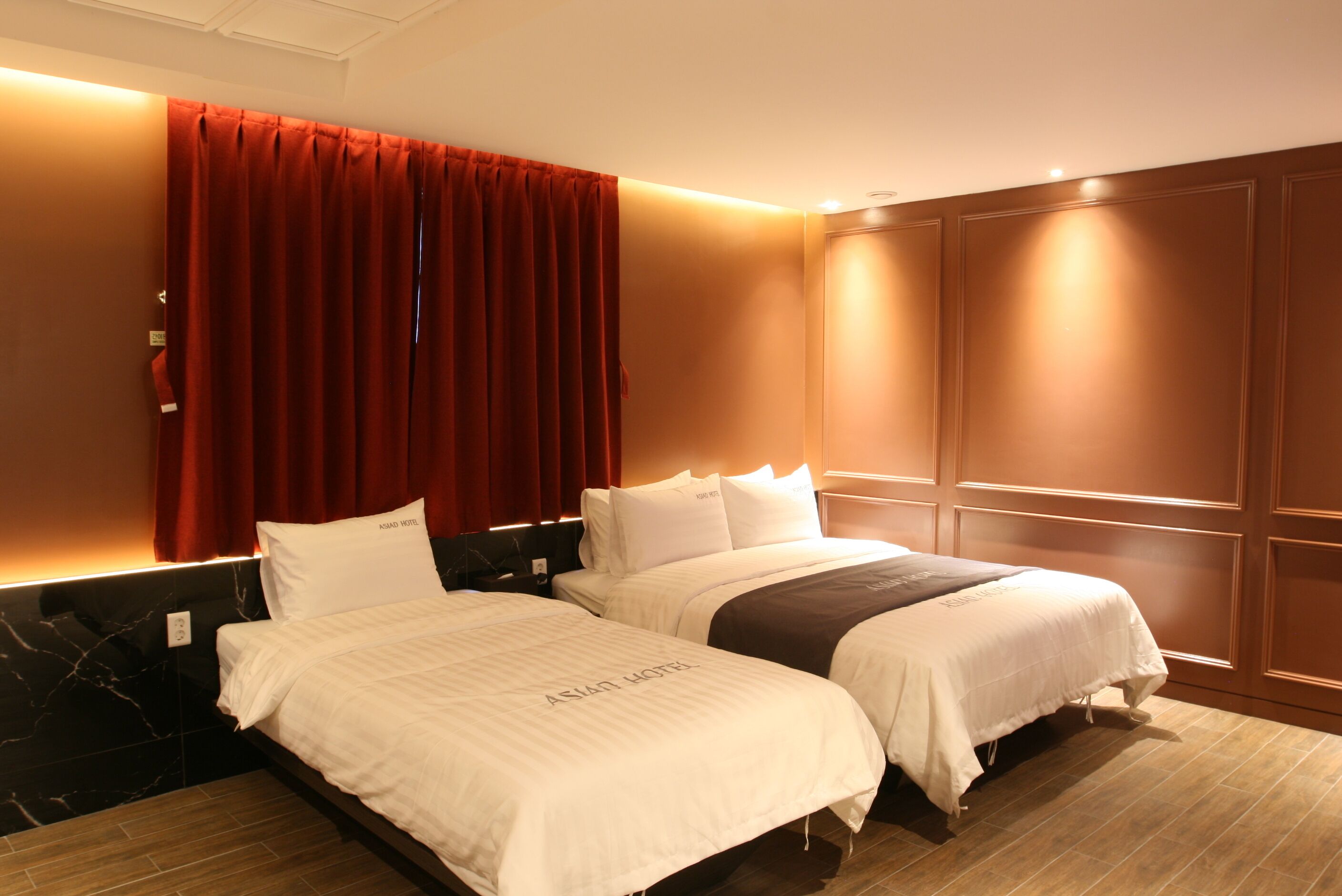 A hotel room with two beds, a red curtain, and a wooden panel wall.