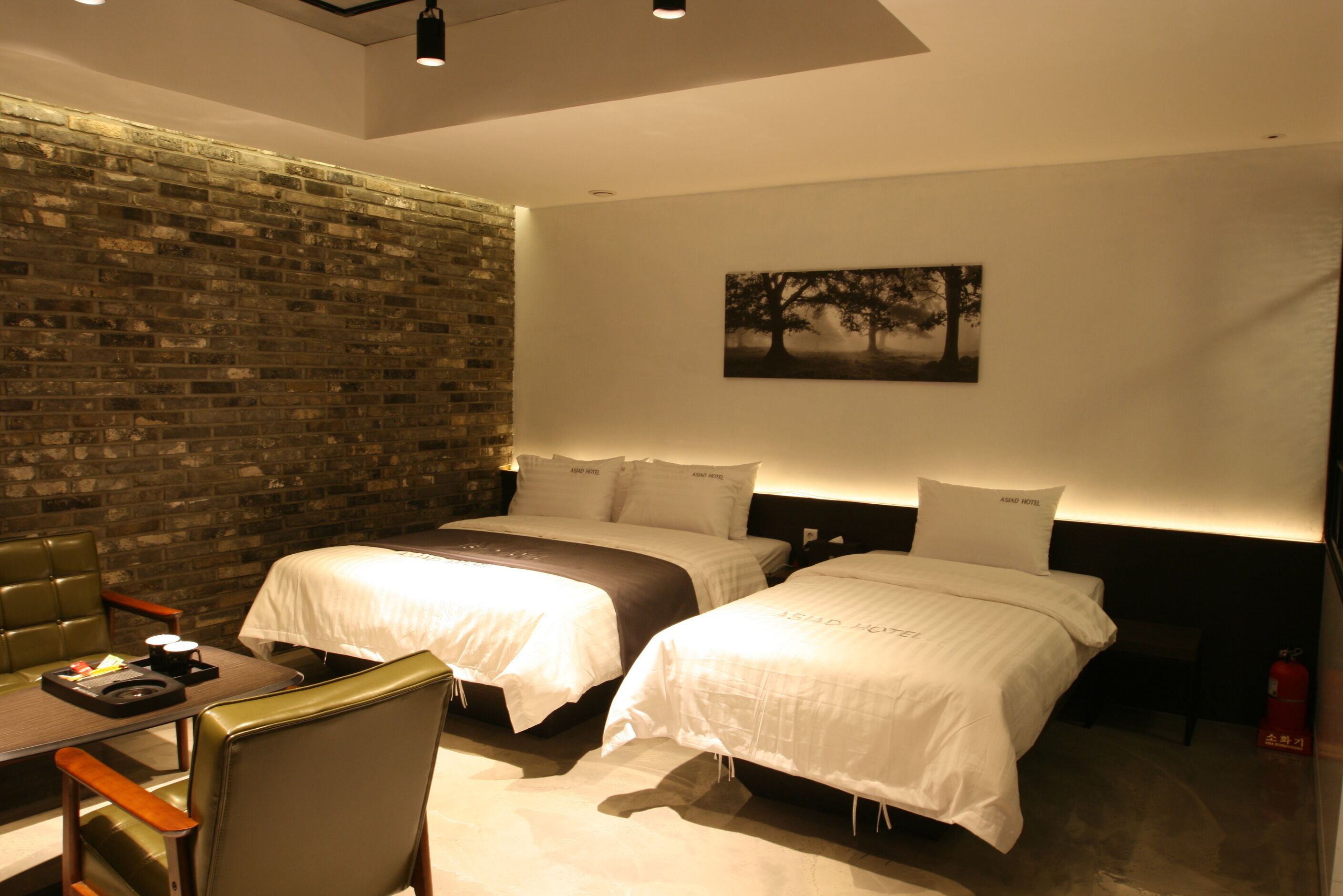 Ein Hotelzimmer mit zwei Betten, einer Ziegelwand, einem Gemälde und einem Tisch mit einem Stuhl.