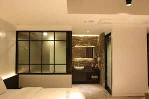 A modern hotel room with a large bed, a bathroom with a stone wall, and a small sink.