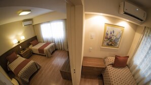 A hotel room with two single beds, a small wooden bench, a wall-mounted air conditioner, and a framed floral artwork. - Hotel Felipe II (Córdoba)