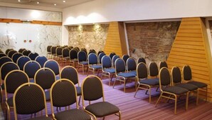A conference room with rows of chairs, a stone wall, and a wooden sloped ceiling. - Hotel Felipe II (Córdoba)