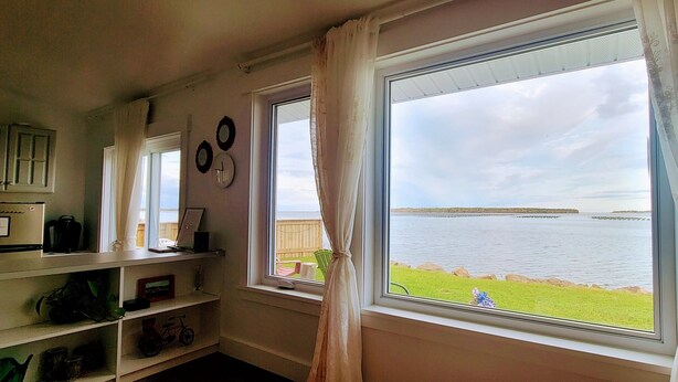 A room with large windows overlooking a body of water, a shelf with various items, and a clock on the wall. - Cabin on the clouds. (Cocagne)