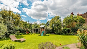 Un jardin avec une cabane en bois, un toboggan, une balançoire et une chaise longue.