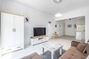 A modern living room with a TV, sofa, and coffee table. There is a kitchen area in the background with a dining table and chairs. - Luxury apARTment By The Sea + FREE PARKING+HBO+Netflix (Varna)
