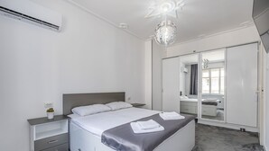 Une chambre moderne avec un grand lit, une table de chevet, une commode, un dressing et un luminaire au plafond.