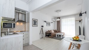 Une cuisine moderne avec des meubles blancs, un four à micro-ondes et un évier. On y trouve un coin repas avec une table et des chaises blanches, ainsi qu’un canapé avec une table basse.