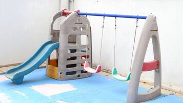 Children can play safely on the blue mat in this play area featuring a slide and colorful swings.