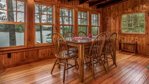 A wooden dining room with a large table and chairs, large windows with a view of trees and a body of water.