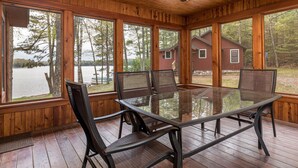 A wooden cabin with a glass dining table and chairs, large windows, and a ceiling fan.